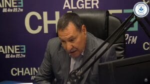 Homme en studio radio avec logo algérien, parlant dans un micro.