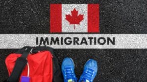 Chaussures et sac à dos sur une route avec drapeau canadien et mot 'Immigration'.