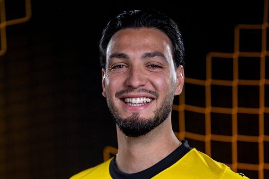 Ramy Bensebaïni souriant en maillot de football jaune.