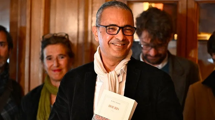 Kamel Daoud souriant avec le prix Goncourt 2024 à la main.