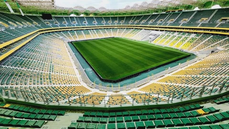 Stade de football vide avec terrain vert et sièges colorés.