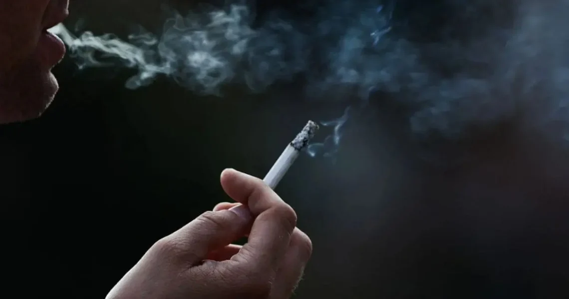 Main tenant une cigarette avec de la fumée dans l'obscurité.