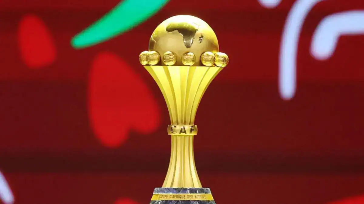 Trophée de la CAN 2025 devant un fond rouge et vert.