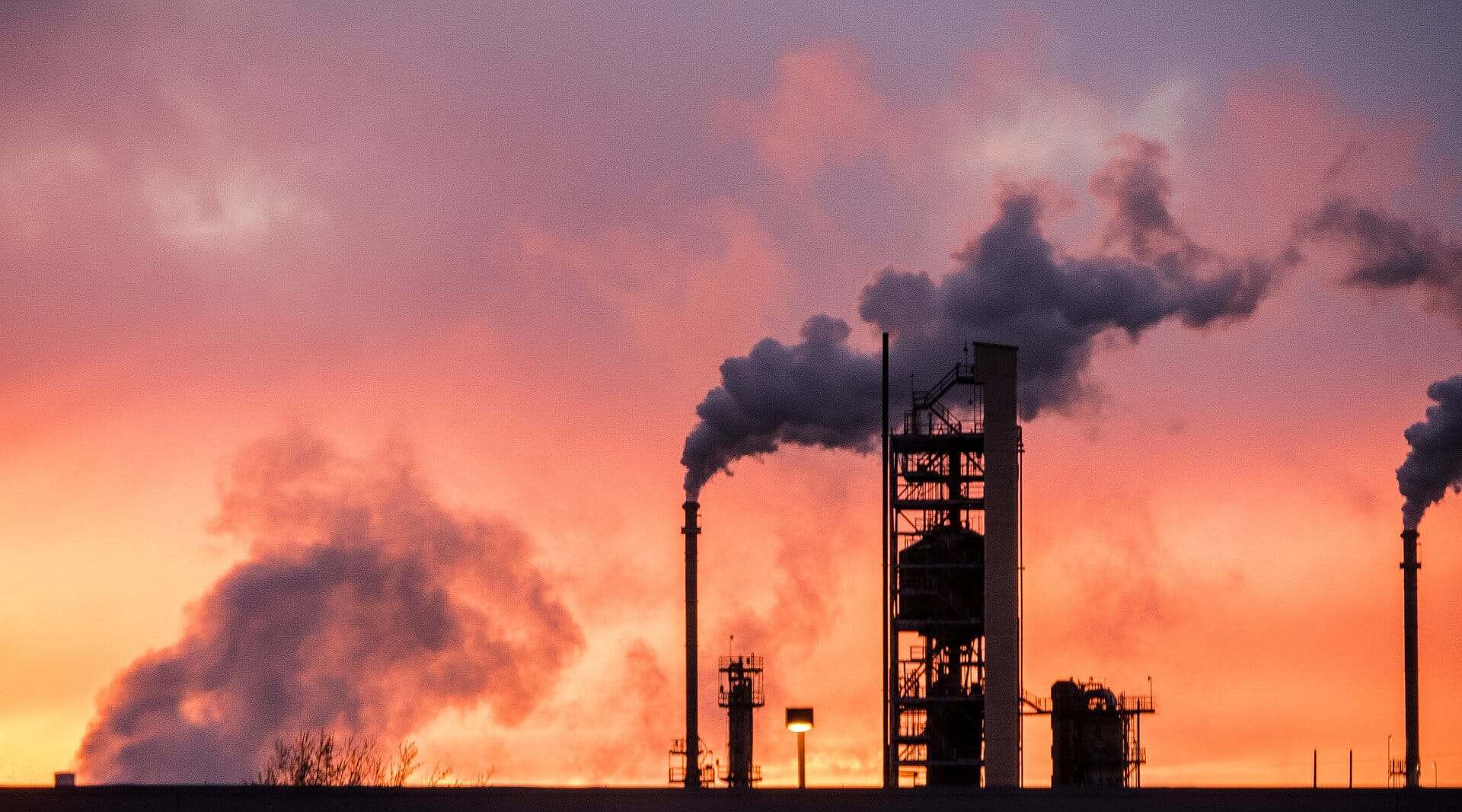 Fumée industrielle s'élevant dans le ciel au coucher du soleil.