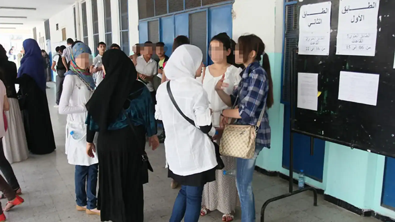 Étudiants et enseignants discutant devant un tableau d'affichage scolaire.