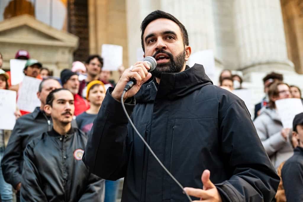 Homme parlant lors d'une manifestation avec une foule en arrière-plan.
