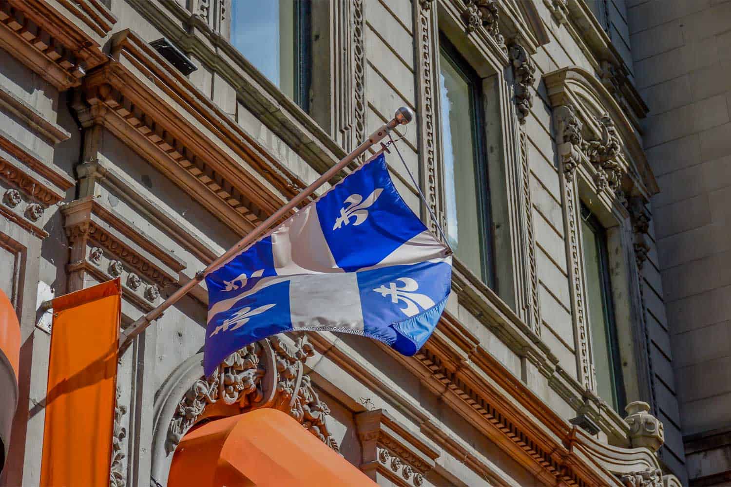 Changement majeur en immigration au Québec dévoilé Drapeau du Québec flottant devant un bâtiment historique.
