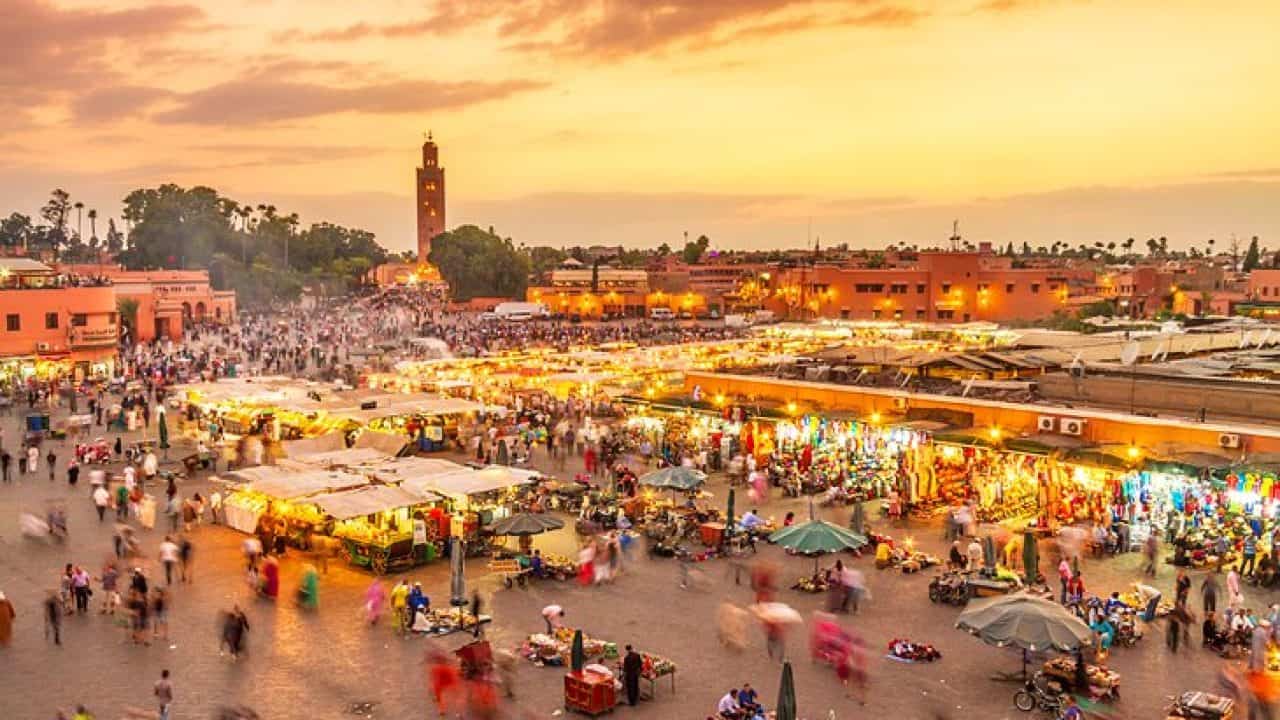 Marché animé au Maroc avec stands et visiteurs au coucher du soleil.