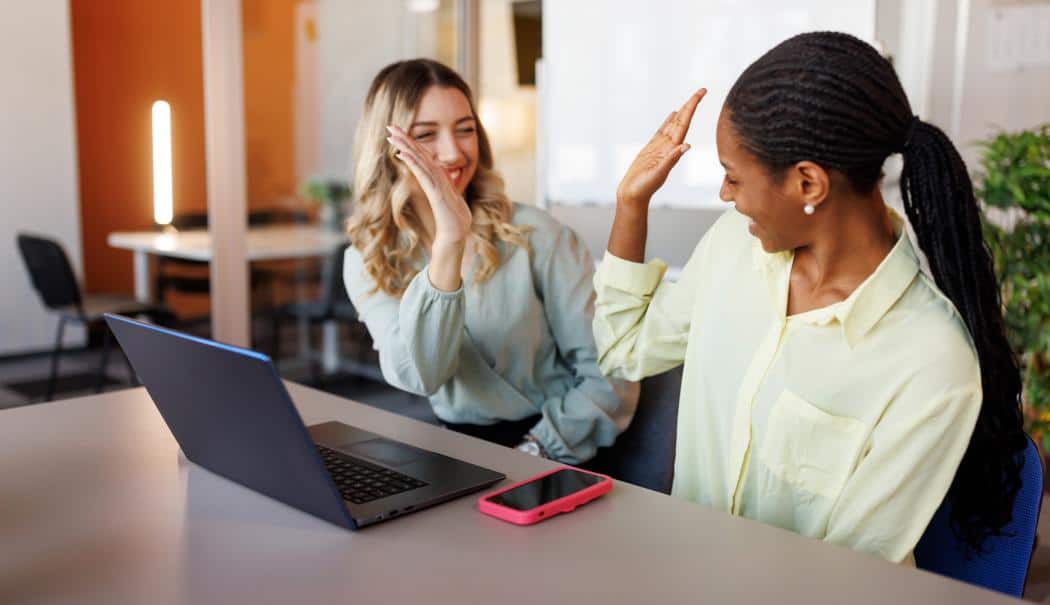 Nouvelles règles : impact sur les frais pour étudiants étrangers Deux jeunes femmes discutant et se félicitant dans un espace de travail moderne.