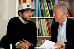 Expulsion controversée : un Algérien malade face à l'OQTF Deux hommes discutent dans une bibliothèque avec des livres en arrière-plan.