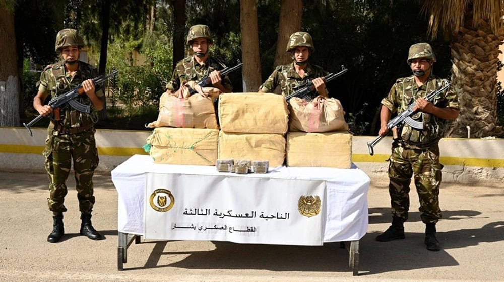 Soldats armés algériens devant des sacs de drogue saisie.