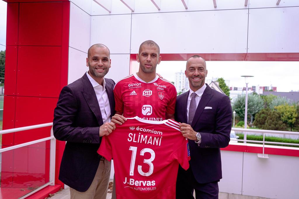 Voici pourquoi Slimani a choisi Brest Slimani pose avec deux hommes en costume et son maillot de football à Brest.