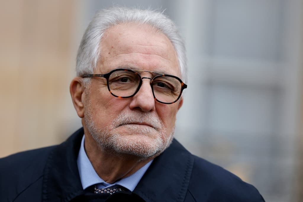 Homme âgé avec lunettes et expression sérieuse.