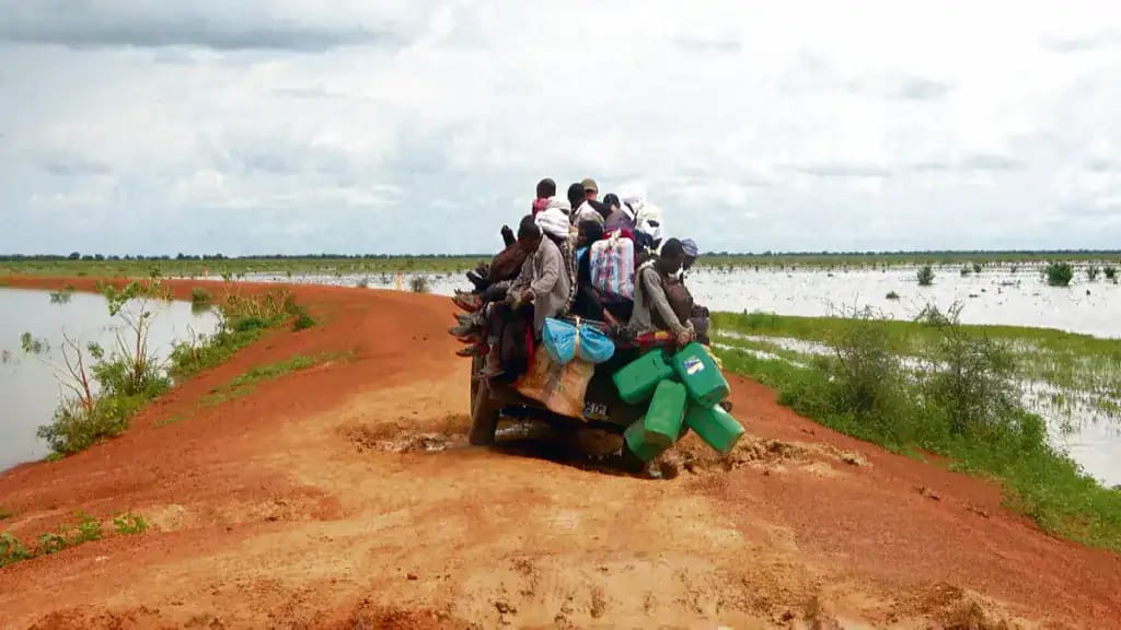 Groupe de migrants transportés sur un véhicule dans un paysage saharien.