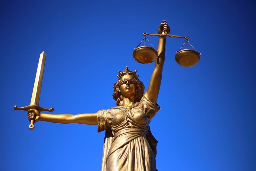 Statue de la Justice dorée avec balance et épée contre ciel bleu.