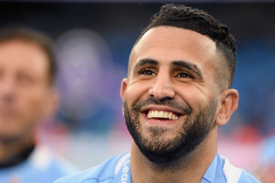 Riyad Mahrez souriant en tenue de football sur le terrain.