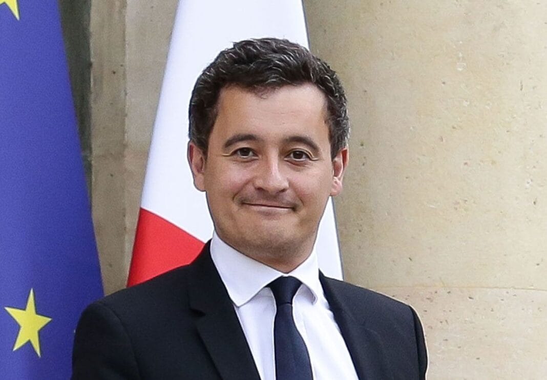 Tensions France-Algérie : Darmanin cible les passeports diplomatiques Homme en costume avec drapeaux France et UE en arrière-plan.