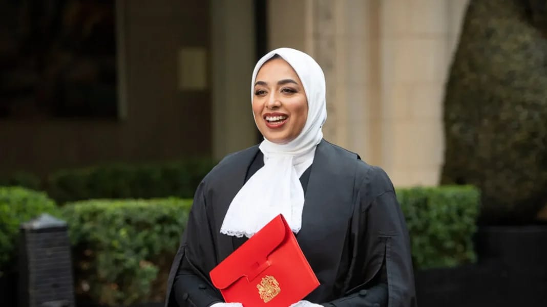 Avocate voilée souriante portant un sac rouge avec un symbole doré.