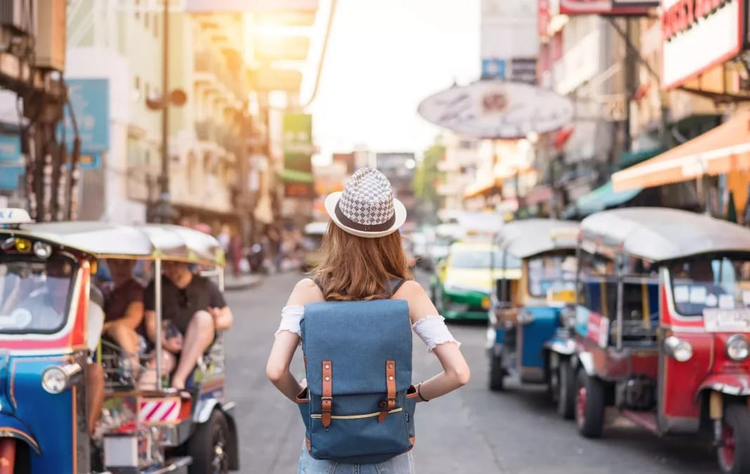 Femme avec sac à dos dans une rue bondée de tuk-tuks et boutiques.