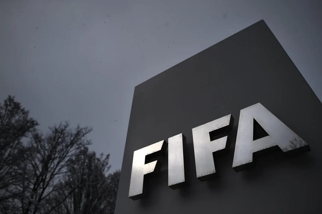 Classement FIFA : l’Algérie dépasse le Cameroun, le Maroc reste fixe Logo de la FIFA sur un panneau en extérieur, ciel nuageux.