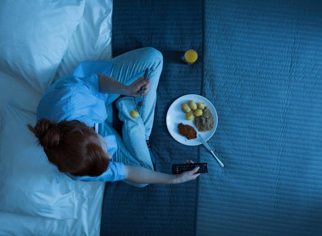 Incroyable : Si vous aimez manger tard, lisez cet article… Femme regardant la télévision dans la chambre avec un plateau de snacks.