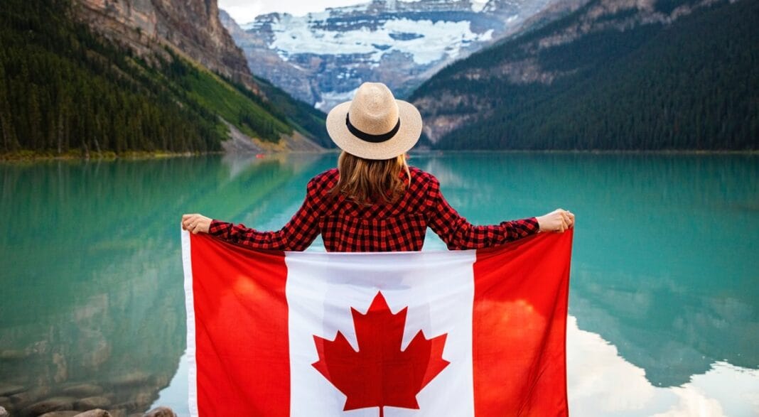 Voyage vers le Canada : voici les semonces d’une avocate Femme avec drapeau canadien devant un lac de montagne.