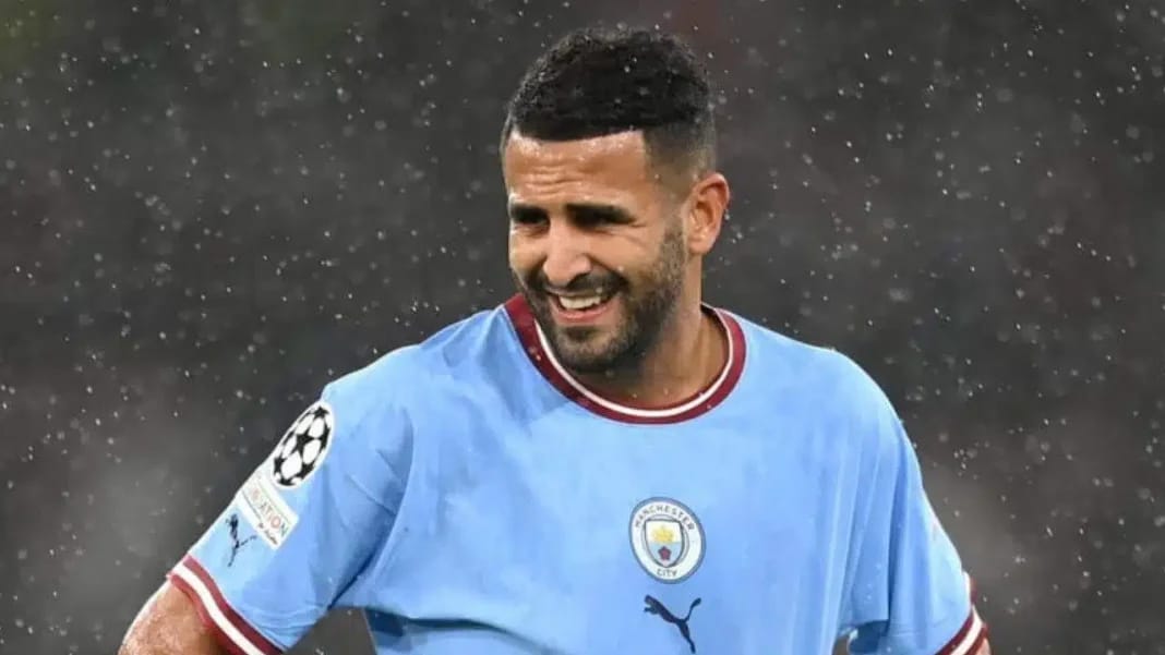 Riyad Mahrez souriant en tenue de football sous la pluie.