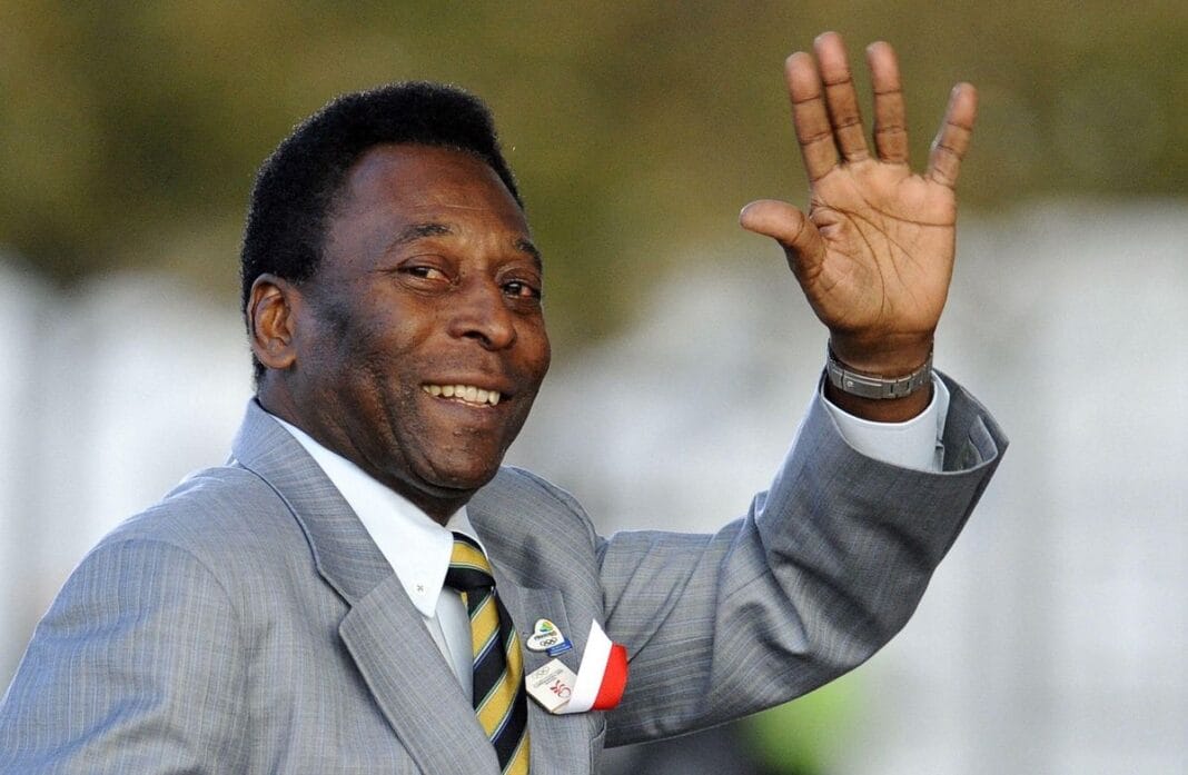 Pelé saluant avec un sourire, en costume gris et cravate.