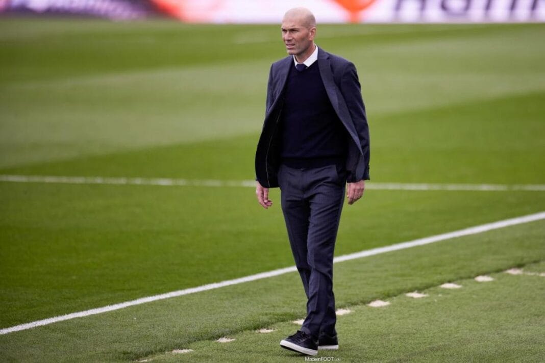 Zidane marchant sur le terrain de football en costume.