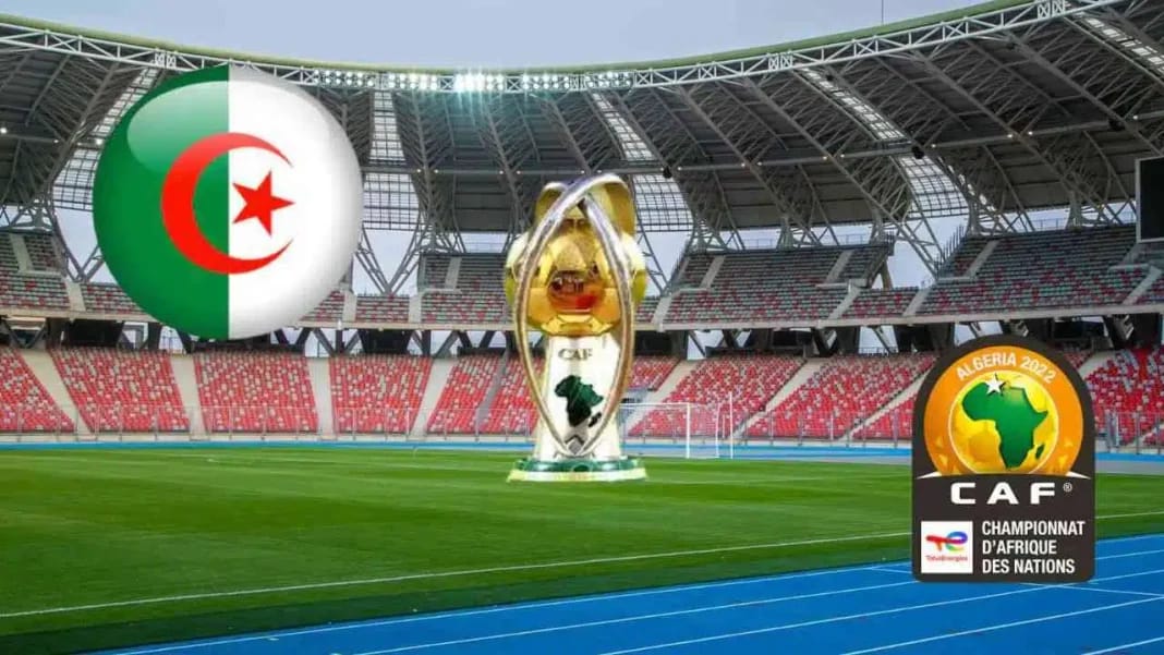 CHAN 2024 : Vers un retrait de l’équipe d’Algérie ? Un dilemme pour la FAF Stade de football en Algérie avec le trophée de la CAN 2023 et drapeau algérien.