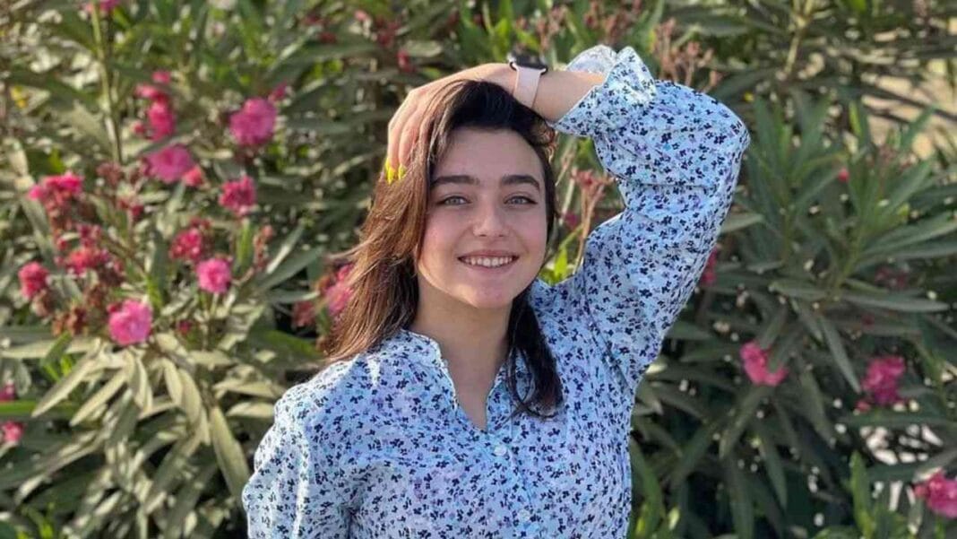 Algérie : Inès Abdelli mariée à 16 ans ? L’actrice livre la vérité. Inès Abdelli souriante avec un fond de fleurs roses et vertes.