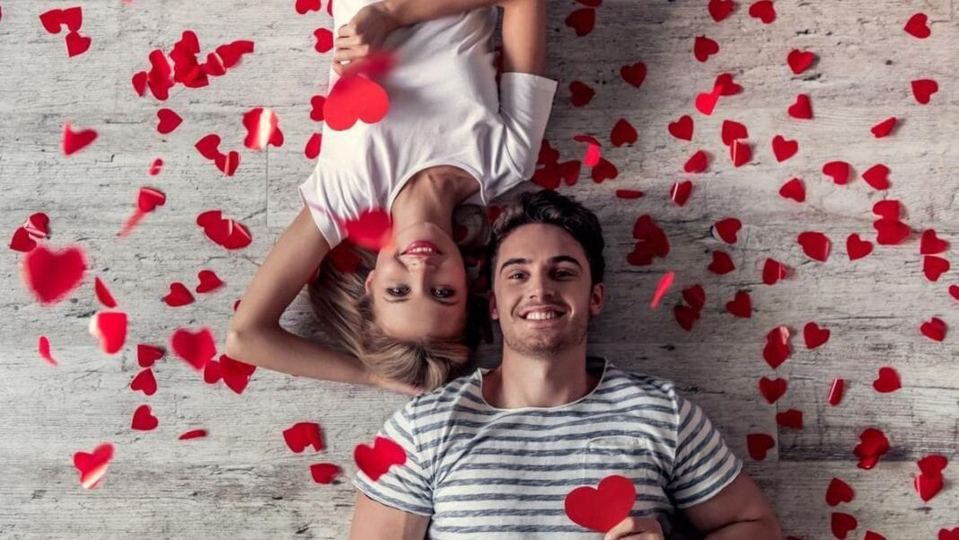 Jeune couple heureux entouré de cœurs en papier rouge pour la Saint-Valentin.
