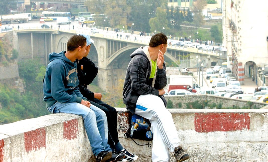 Jeunes hommes assis sur un mur à Alger, semblant préoccupés.