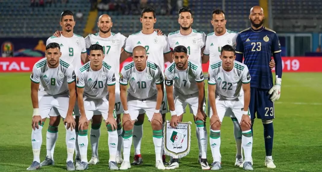 Groupe de joueurs de football algériens en tenue officielle sur le terrain.