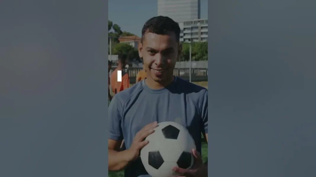 Jeune homme souriant tenant un ballon de football en plein air.