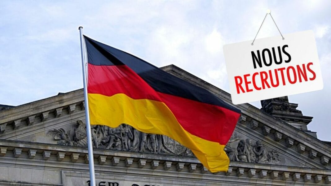 Recrutement de gardes de sécurité par l’ambassade d’Allemagne à Alger : Opportunité professionnelle en Algérie Drapeau allemand devant un bâtiment officiel avec panneau de recrutement.
