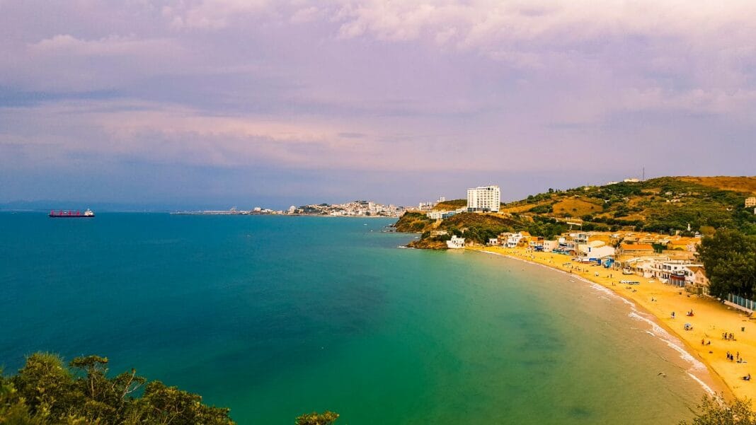 Vue panoramique d'une plage algérienne avec mer et côte en arrière-plan.