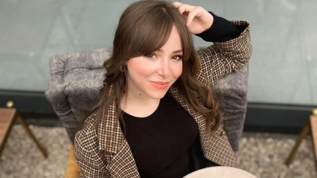 Jeune femme avec cheveux bruns et sourire charmant, assise dans un fauteuil.