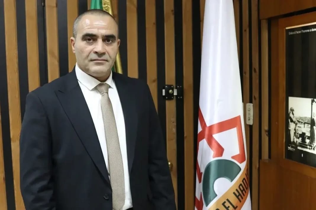 Karim Boulaioune en costume, devant le drapeau du complexe Sider El Hadjar.