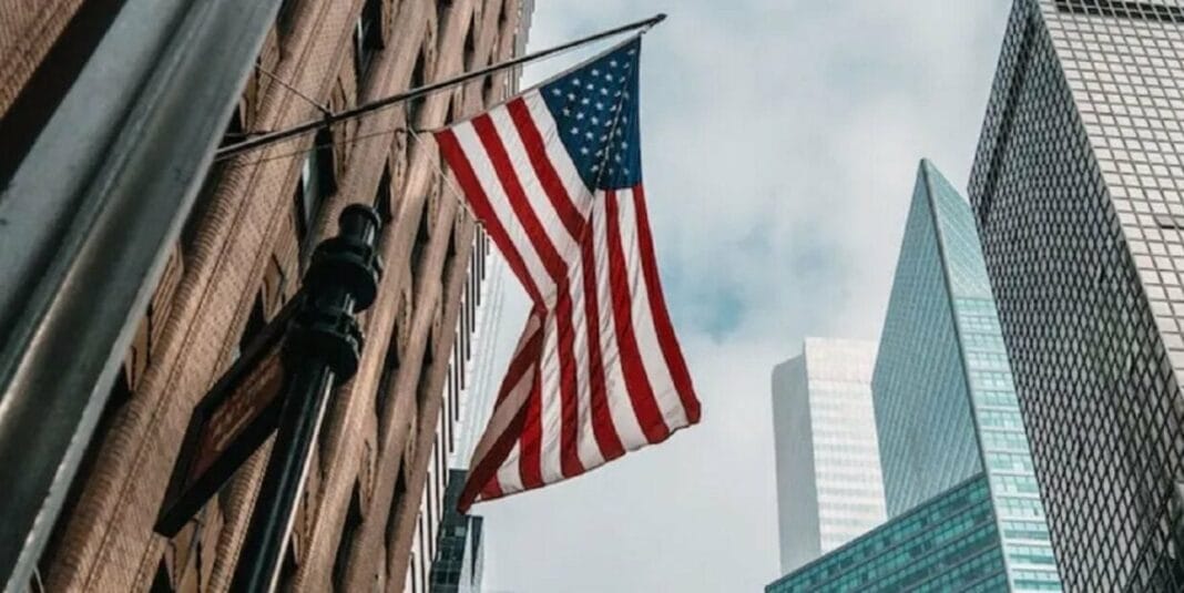 Drapeau américain flottant devant des gratte-ciel modernes.