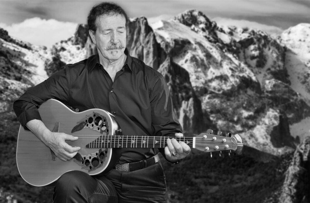 Lounis Aït Menguellet au Canada : Deux Concerts Exceptionnels en Mai 2024 Lounis Aït Menguellet jouant de la guitare dans un paysage montagneux.