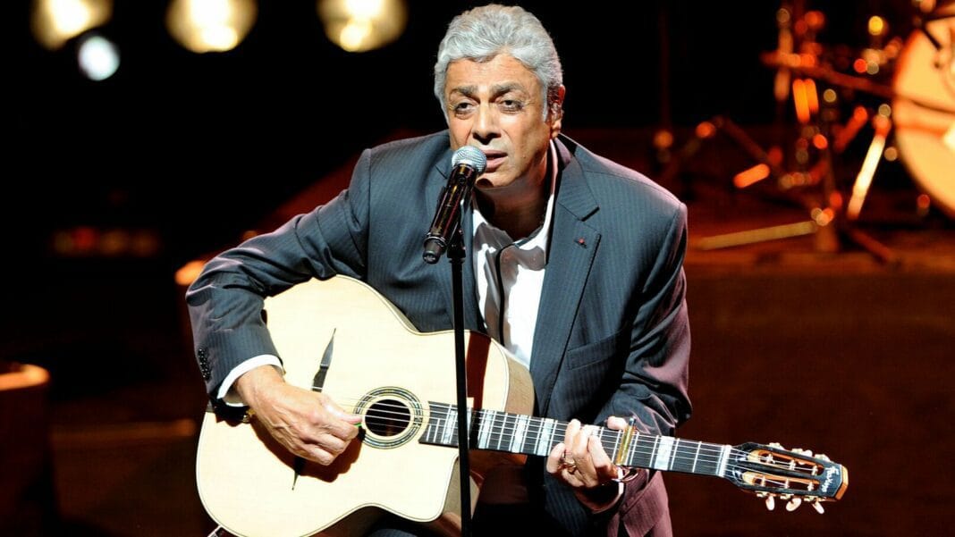 Enrico Macias joue de la guitare lors d'un concert en direct.