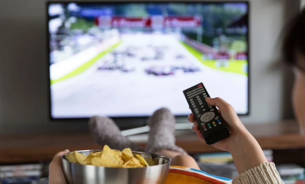 Personne regardant la télévision avec une télécommande et un bol de chips.