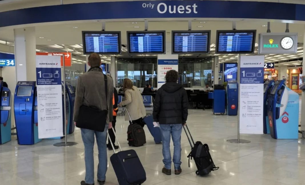 Voyageurs à l'aéroport d'Orly avec valises et écrans d'information.