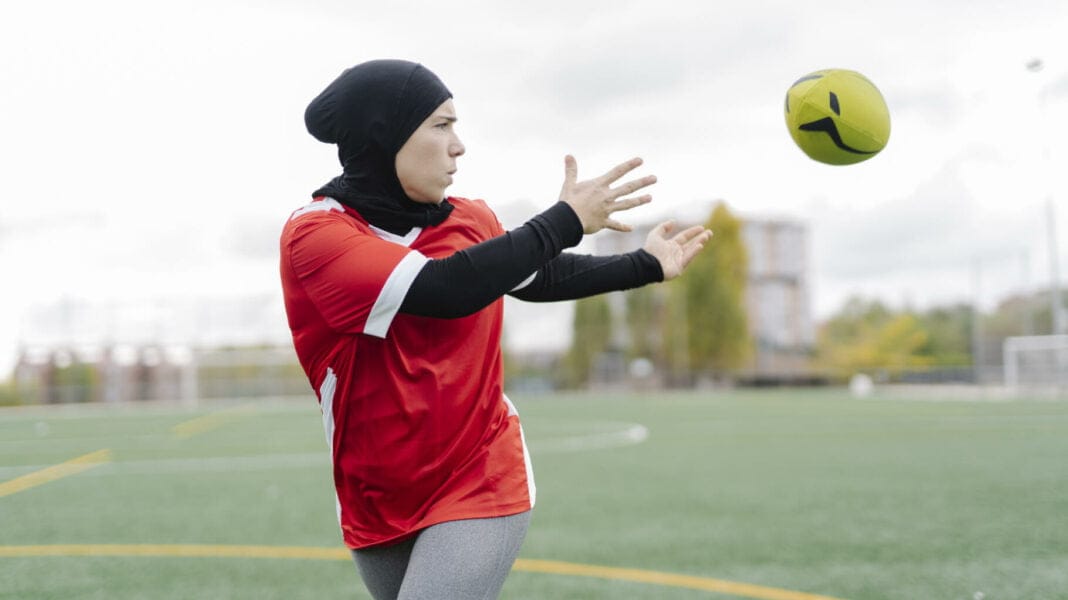 JO Paris 2024 : Amnesty International conteste l’interdiction du voile aux athlètes musulmanes Femme musulmane en hijab jouant au football sur un terrain.