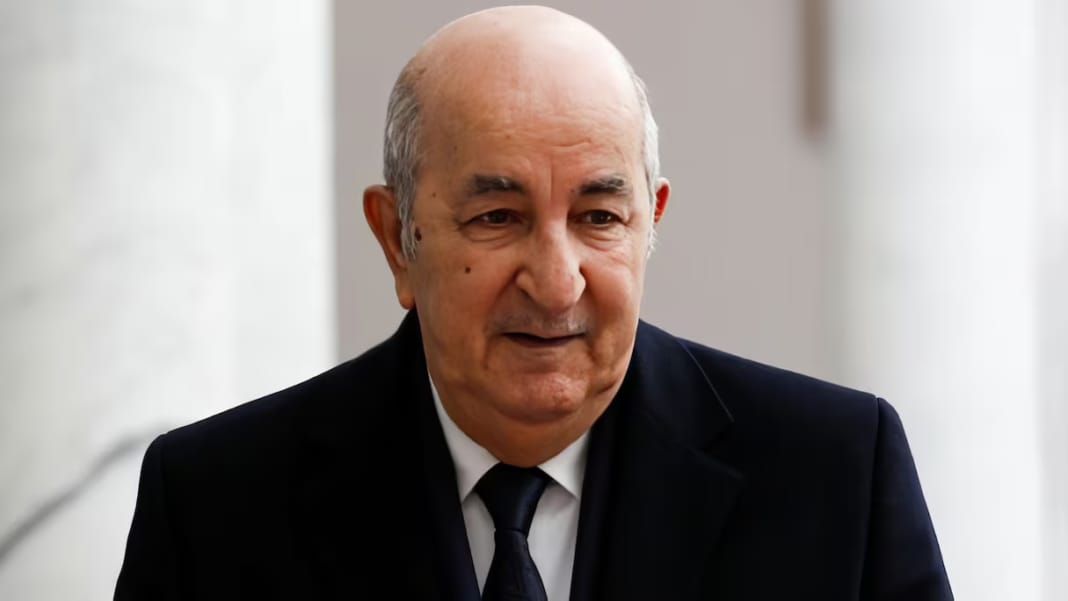 Homme politique algérien en réunion, visage sérieux, costume noir.