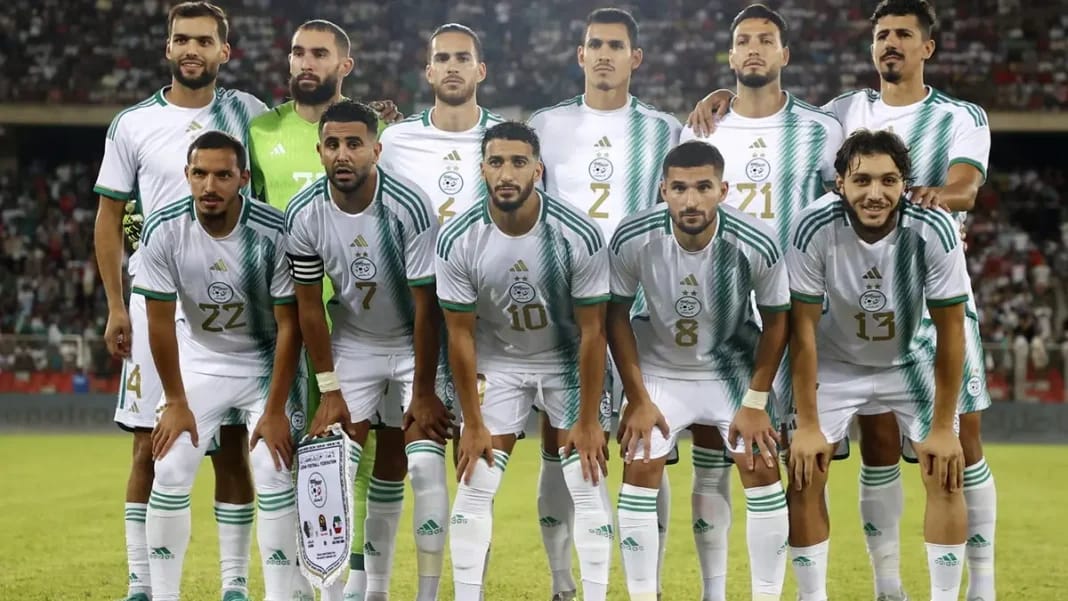 Groupe de joueurs de football algériens en tenue blanche sur le terrain.