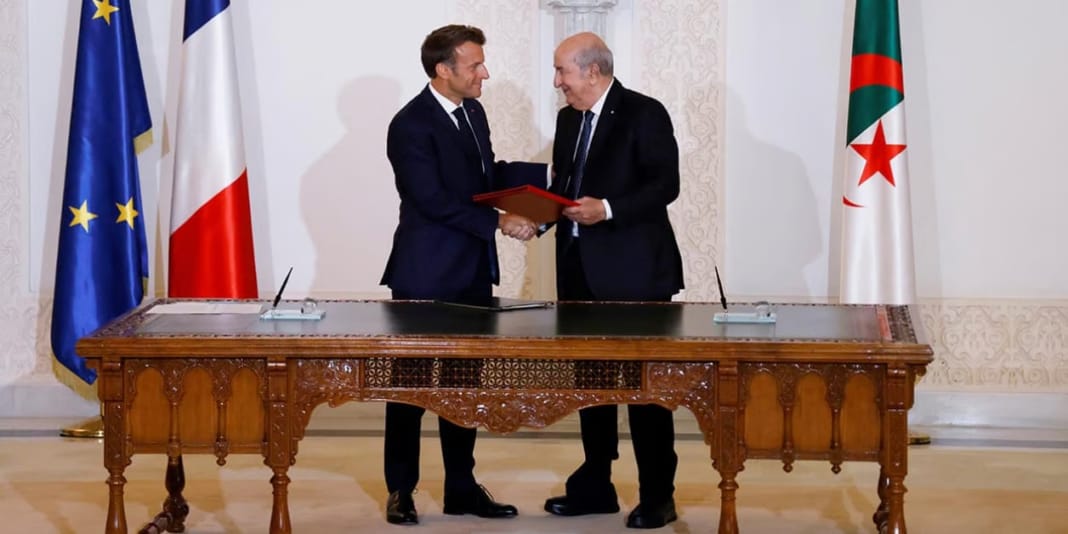 Controverse en France : L’aide française à l’Algérie au cœur d’un débat enflammé Deux hommes signent un accord officiel dans une salle élégante.
