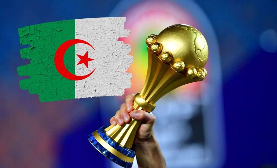 Qualif CAN 2025- Algérie vs Togo : date, heure,stade… Joueur algérien tenant la coupe d'Afrique 2025 avec drapeau algérien en arrière-plan.