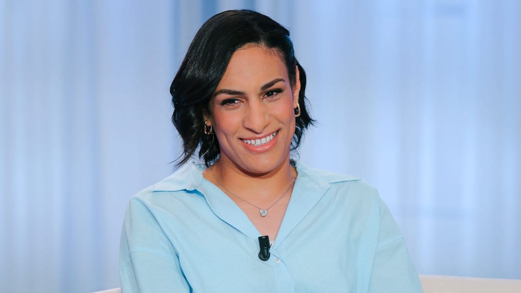 Imane Khelif souriante, vêtue élégamment, dans un décor moderne.